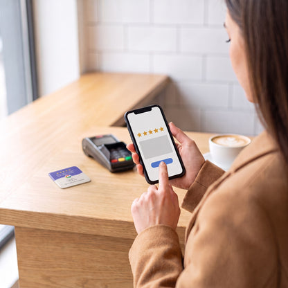 Kundin gibt am Handy eine Sternebewertung ab, die NFC-Karte liegt auf der Theke | English