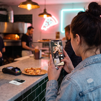 Kundin sieht sich am Handy ein Video der Pizzeria an | English